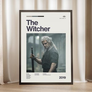 May include: A framed poster featuring a minimalist design for The Witcher television series. The print includes the title, the year 2019, production credits, and a central photographic image of a long-haired character holding a sword.