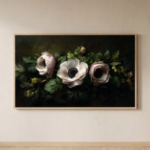 Puede incluir: Una impresión de arte mural rectangular que presenta un arreglo horizontal de tres grandes flores de anémona de color rosa pálido con centros oscuros, rodeadas de follaje verde intenso y capullos, sobre un fondo oscuro en un marco de madera clara.