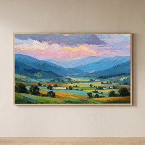 May include: A framed landscape painting showing a valley scene with rolling hills and mountains. The sky transitions from pink and orange to purple. The foreground features green and yellow fields, with trees and small buildings.