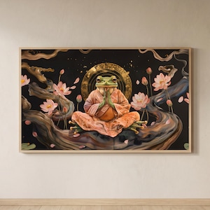Op de afbeelding: Een ingelijste kunstdruk met een mediterende kikker in een perzikkleurige robe, handen gevouwen in gebed. De kikker zit op een tak met roze lotusbloemen tegen een zwarte achtergrond. Een gouden halo en sierlijke details completeren de spirituele scène.