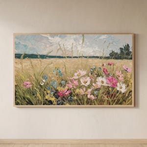 Pode incluir: Uma pintura de paisagem retangular numa moldura de madeira clara, apresentando um campo texturizado de trigo dourado e ervas altas, intercalado com flores silvestres cor-de-rosa, brancas e azuis sob um céu nublado com horizonte escuro.