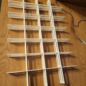 Può includere: Un organizer per scaffali in plastica bianca con un design a griglia. L'organizer è composto da pezzi ad incastro, creando molteplici scomparti rettangolari. Il design è semplice e funzionale, adatto per organizzare oggetti.