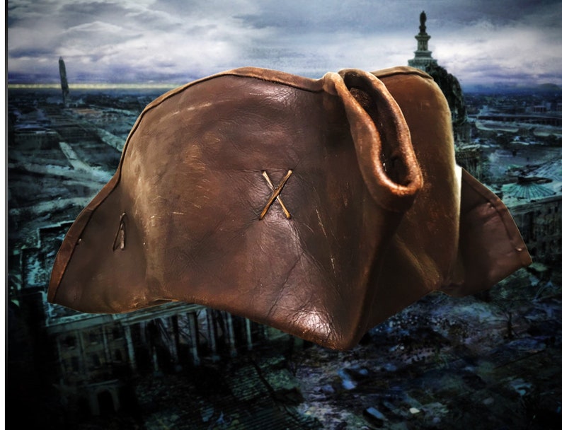 May include: A brown leather pirate hat with a stitched X on the front. The hat is worn and has a distressed look.