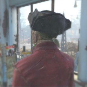 May include: A person wearing a red jacket and a black hat with a brim. The person is standing in front of a window with a view of a city street.