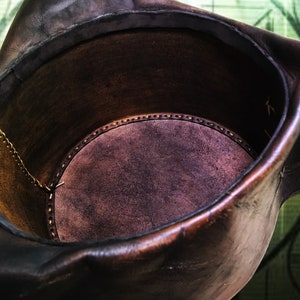 May include: A brown leather bucket with a suede lining. The bucket has a stitched seam around the top edge.