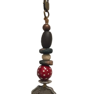 May include: A silver charm with a wolf design hangs from a brown cord with a variety of colorful beads, including a red bead with white polka dots.