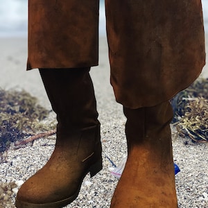 May include: A pair of brown suede boots with a fold-over cuff. The boots are worn and have a distressed look.