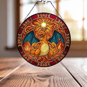 May include: Round stained glass window featuring a Charizard design. The artwork showcases an orange Charizard with blue wings, set against a fiery background and a sun. The window is framed with red and gold accents, and is suspended by a chain.