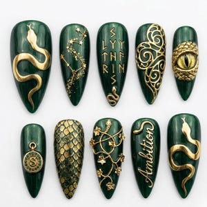 May include: A set of ten emerald green nail designs with gold accents. The designs include snakes, constellations, and the word "Ambition". Each nail has a unique design, showcasing intricate details and textures.