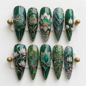 Può includere: Un set di dieci unghie finte a mandorla con intricati disegni in stile vetrata colorata verde e bianco. Le illustrazioni includono fiori di loto, ninfee e pesci koi, accentuati da linee argentate metallizzate su una finitura lucida.