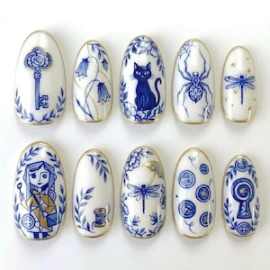 May include: A set of ten oval-shaped, white artificial nails with intricate blue and gold designs. The designs include a key, flowers, a cat, a spider, a dragonfly, a girl, a spool of thread, buttons, and a keyhole.
