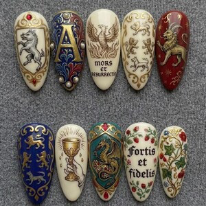 K&ouml;nnte beinhalten: Eine Sammlung von zehn aufwendig gestalteten Nagelkunstwerken. Jeder Nagel zeigt ein einzigartiges Design, darunter heraldische Symbole, ein Ph&ouml;nix und florale Muster. Die Farben umfassen Gold, Rot, Blau und Creme, mit detaillierten Kunstwerken und Text.