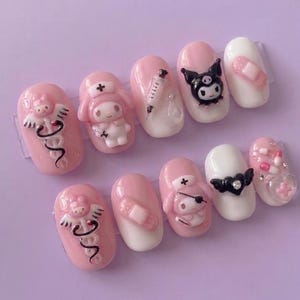 May include: A set of ten artificial nails in various designs. The nails feature a light pink base with white accents. Some nails have 3D embellishments of cartoon characters, medical symbols, and bandages. The overall aesthetic is cute and playful.