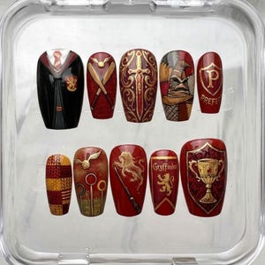 Può includere: Un set di dieci unghie finte con dettagliati disegni dipinti a mano ispirati alla casa di Grifondoro. Le unghie presentano motivi che includono un'uniforme scolastica, un boccino d'oro, una spada, un cappello parlante, un distintivo da prefetto, un leone e una coppa.