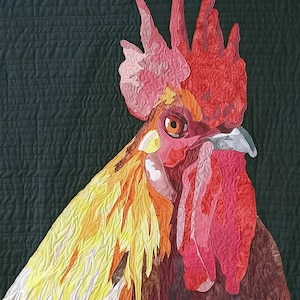 Pode incluir: Um close-up da cabeça e pescoço de um galo, feito de tecido e acolchoado. O galo é marrom, vermelho, laranja e amarelo. A crista e as barbelas do galo são vermelhas.