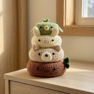 May include: A stack of four crocheted animal shapes: a brown base with a smiling face, a tan bear, a cream-colored bunny, and a green bird with a leaf. The handmade toys are stacked on top of each other.
