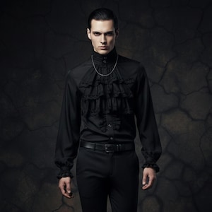 Puede incluir: Camisa negra de manga larga con cuello alto y puños con volantes. La camisa presenta un diseño de volantes en capas en la parte delantera y se combina con pantalones negros y un cinturón. Un collar de cadena plateada añade un acento sutil.