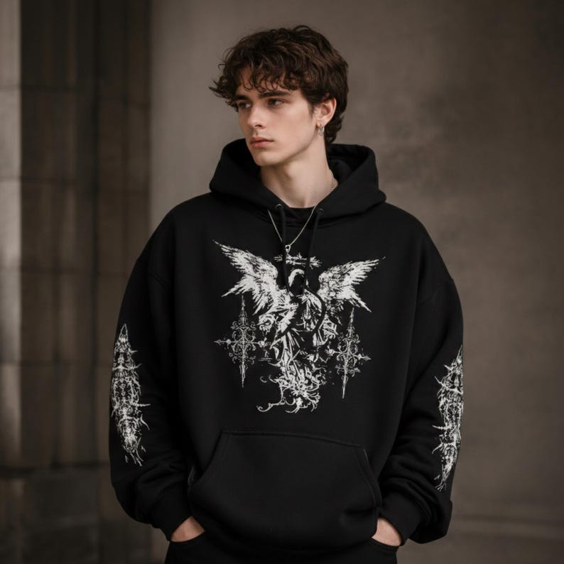 May include: Black hooded sweatshirt with a large white graphic on the front featuring an angel with outstretched wings and ornate details. Additional white designs are on the sleeves. The sweatshirt has a front pocket.