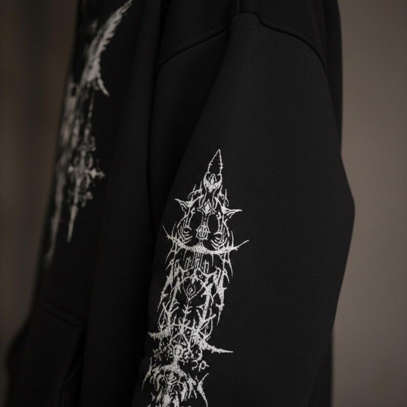 May include: Black hoodie with white, gothic-style graphic designs on the sleeves and upper chest. The intricate, spiky artwork creates a striking contrast against the solid black fabric. The design has a dark, edgy aesthetic.