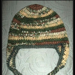 May include: A crocheted hat with a camouflage pattern and long, braided ties. The hat is made with brown, green, and beige yarn.