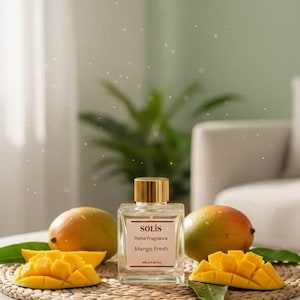 Könnte beinhalten: Ein quadratischer Glasflakon "SOLIS Home Fragrance Mango Fresh" mit goldenem Verschluss, umgeben von ganzen und geschnittenen Mangos. Der Flakon steht auf einer gewebten Matte. Die Szene ist auf einer weißen Oberfläche.