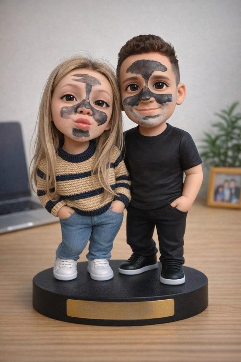 May include: A figurine of a couple with charcoal face masks. The woman wears a striped sweater, jeans, and white sneakers. The man is in a black shirt, pants, and shoes. They stand on a black base with a gold nameplate.