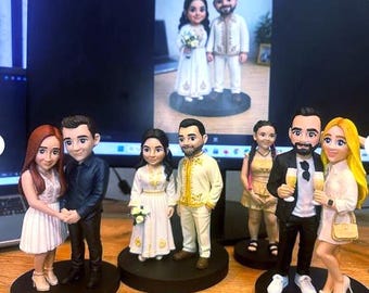 May include: Three pairs of custom bobblehead figurines stand on black circular bases. The figures depict couples in various outfits, including a white dress and dark shirt, a traditional white and gold ensemble, and formal attire with champagne glasses.
