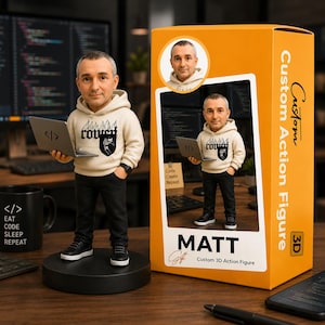 Könnte beinhalten: Eine individuelle 3D-Actionfigur eines Mannes mit Kapuzenpullover und Laptop. Die Figur steht auf einem schwarzen Sockel, mit einer Box mit der Aufschrift "Custom Action Figure" und "MATT". Eine schwarze Tasse mit dem Text "EAT CODE SLEEP REPEAT" ist ebenfalls sichtbar.