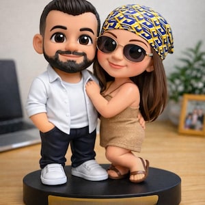 May include: A figurine of a couple, standing close together on a black base. The man wears a white shirt, dark pants, and white sneakers. The woman wears a gold dress, sunglasses, and a patterned headscarf. The figurine is a cartoon style.