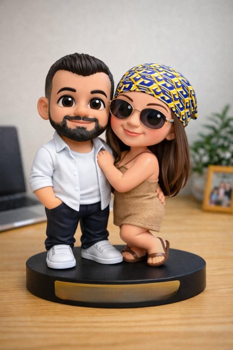 May include: A figurine of a couple, standing close together on a black base. The man wears a white shirt, dark pants, and white sneakers. The woman wears a gold dress, sunglasses, and a patterned headscarf. The figurine is a cartoon style.