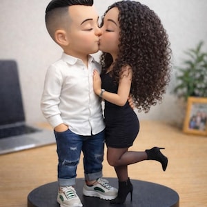 May include: A figurine of a kissing couple. The man wears a white shirt, blue jeans, and sneakers. The woman is in a black dress and high heels. The base is black with a gold trim. The couple is embracing and kissing.