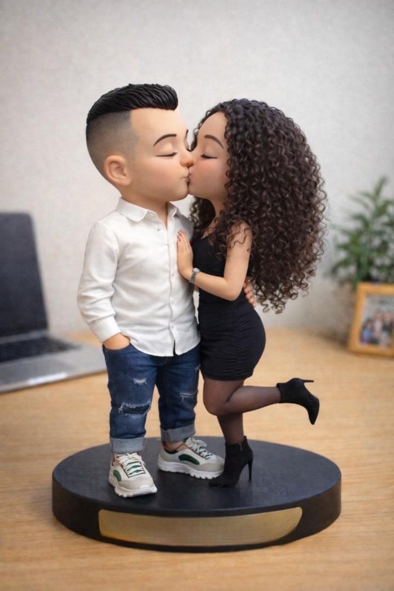 May include: A figurine of a kissing couple. The man wears a white shirt, blue jeans, and sneakers. The woman is in a black dress and high heels. The base is black with a gold trim. The couple is embracing and kissing.