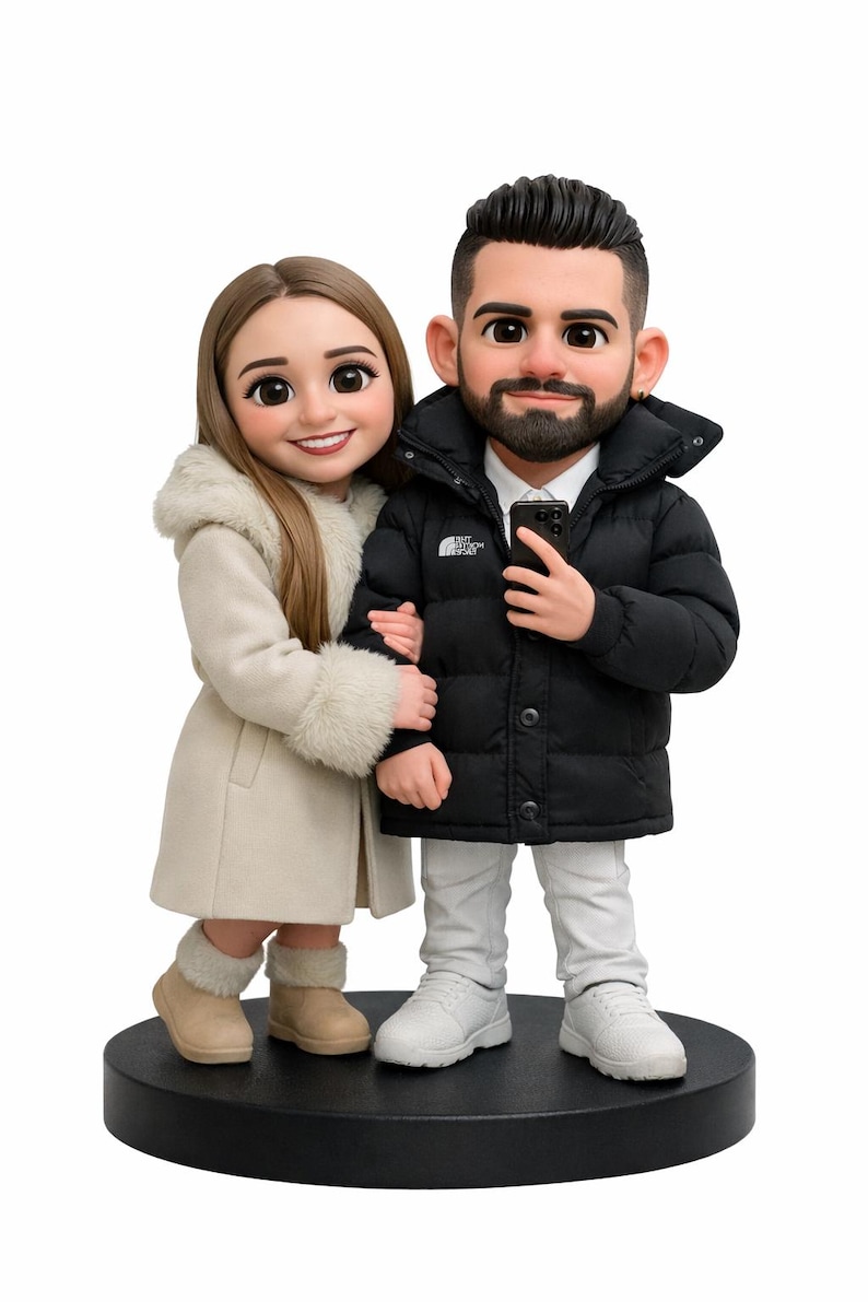 May include: A figurine of a couple, standing close together on a black base. The woman wears a cream-colored coat with a fur-lined hood and boots. The man wears a black puffer jacket and white sneakers. The figurine is a cartoon-like representation.