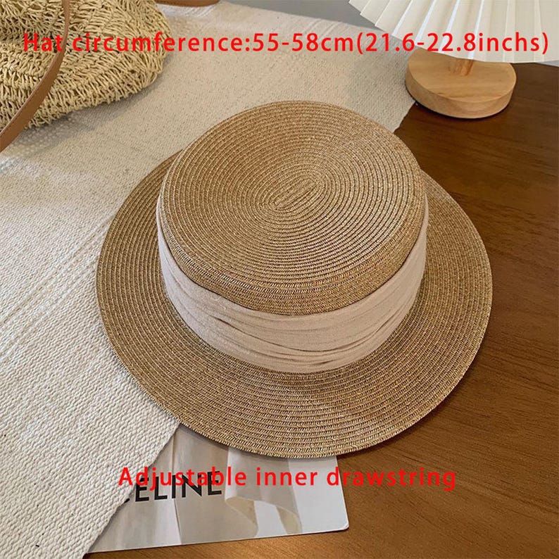 May include: A straw hat with a beige band and a wide brim. The hat has a hat circumference of 21.6-22.8 inches. The hat has an adjustable inner drawstring. The hat is sitting on a white surface.