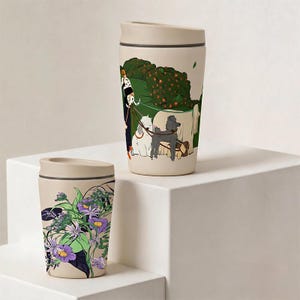 May include: Two beige travel mugs with lids. The taller mug features a graphic illustration of a person walking several dogs in a green park. The shorter mug displays a detailed botanical print with purple flowers, green leaves, and dark accents.