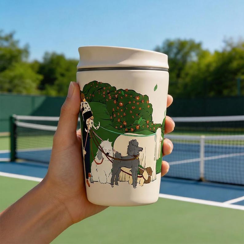 May include: A cream-colored travel mug featuring a colorful illustration of a person walking several dogs of various breeds, including a grey poodle and a white fluffy dog, against a backdrop of green bushes with small red flowers.