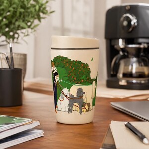 May include: A cream-colored travel mug featuring a colorful illustration of a person walking several dogs of various breeds, including a grey poodle and a white fluffy dog, through a green park with orange flowers and a large beige dog.