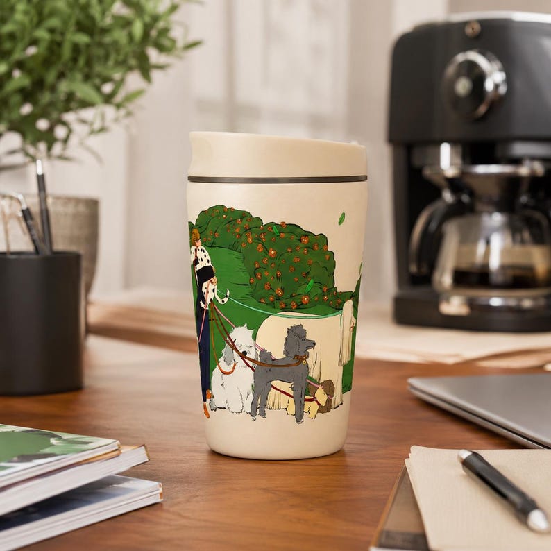 May include: A cream-colored travel mug featuring a colorful illustration of a person walking several dogs of various breeds, including a grey poodle and a white fluffy dog, through a green park with orange flowers and a large beige dog.