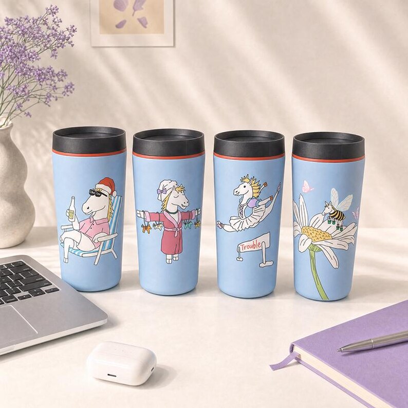 Pu&ograve; includere: Quattro bicchieri da viaggio azzurri con coperchi neri, ognuno con un'illustrazione unica di unicorno. I disegni includono un unicorno con cappello da Babbo Natale, un unicorno in accappatoio, un unicorno ballerina e un unicorno ape su una margherita.