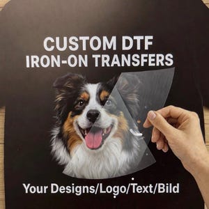 Könnte beinhalten: Ein schwarzes T-Shirt mit einem individuellen DTF-Aufbügeltransfer eines dreifarbigen Hundes mit weißem, braunem und schwarzem Fell. Der Text CUSTOM DTF IRON-ON TRANSFERS und Your Designs/Logo/Text/Bild ist in Weiß um das Motiv gedruckt.