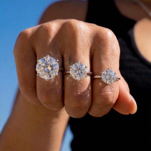May include: Three silver-toned rings, each featuring a single round-cut clear stone held in a six-prong setting. The rings are worn on three adjacent fingers, displaying a noticeable difference in the size of the stones from largest to smallest.