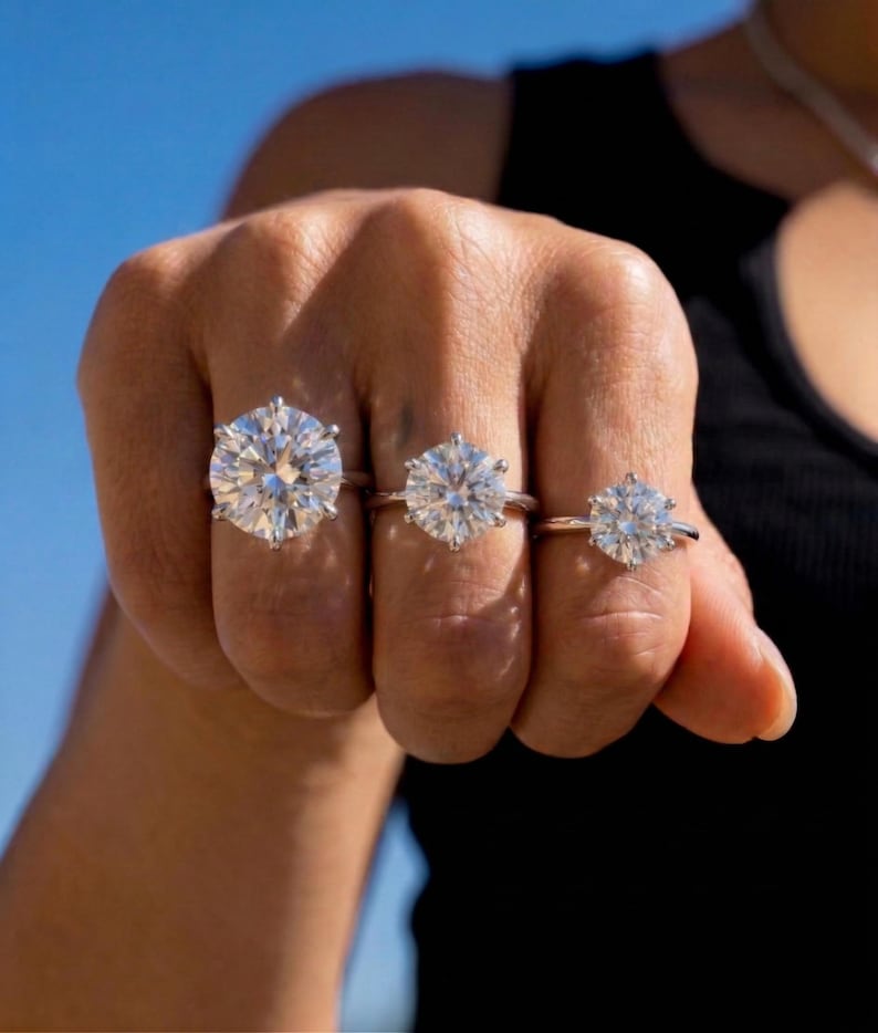 May include: Three silver-toned rings, each featuring a single round-cut clear stone held in a six-prong setting. The rings are worn on three adjacent fingers, displaying a noticeable difference in the size of the stones from largest to smallest.