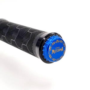 Könnte beinhalten: Schwarzer Fahrradlenkergriff mit strukturiertem Muster. Die Endkappe ist ein blauer Flaschenverschluss mit goldenem Text "Birra Messina". Der Griff ist schwarz und der Hintergrund ist weiß.