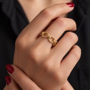 May include: A gold ring featuring a series of interconnected circular links with a textured, beaded surface. The band is constructed from multiple repeating round segments that create a continuous chain-like design around the finger.
