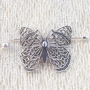 May include: Silver filigree butterfly brooch with a pearl accent. The brooch is attached to a silver pin.