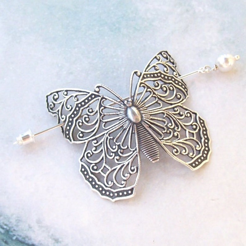 May include: Silver butterfly hair comb with a pearl accent. The butterfly is intricately detailed with a filigree design.
