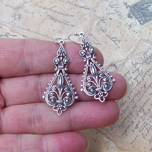 May include: A pair of silver dangle earrings with intricate floral designs and small round beads.