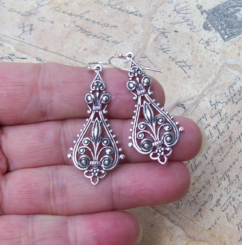May include: A pair of silver dangle earrings with intricate floral designs and small round beads.