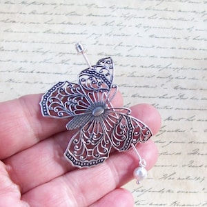 May include: Silver filigree butterfly hair comb with a pearl accent. The butterfly is detailed with intricate designs and has a delicate, feminine look.