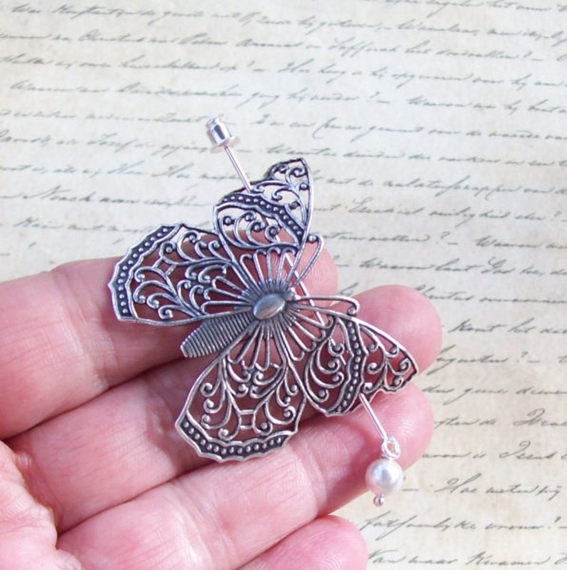 May include: Silver filigree butterfly hair comb with a pearl accent. The butterfly is detailed with intricate designs and has a delicate, feminine look.
